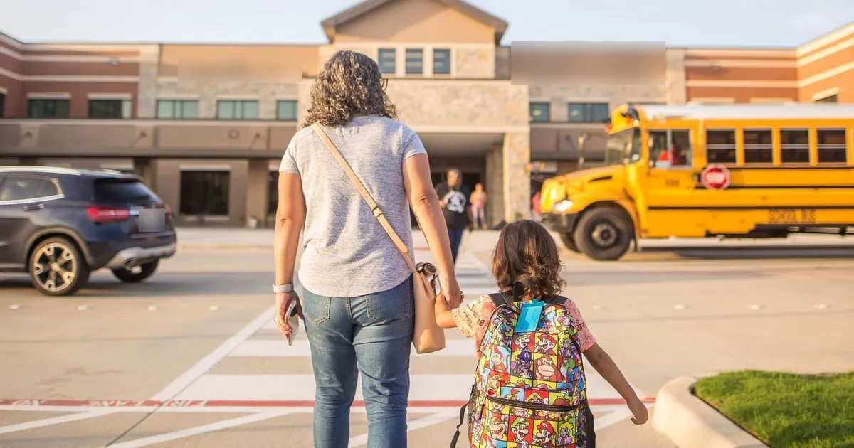 A mother walking her daughter to school past a yellow school bus