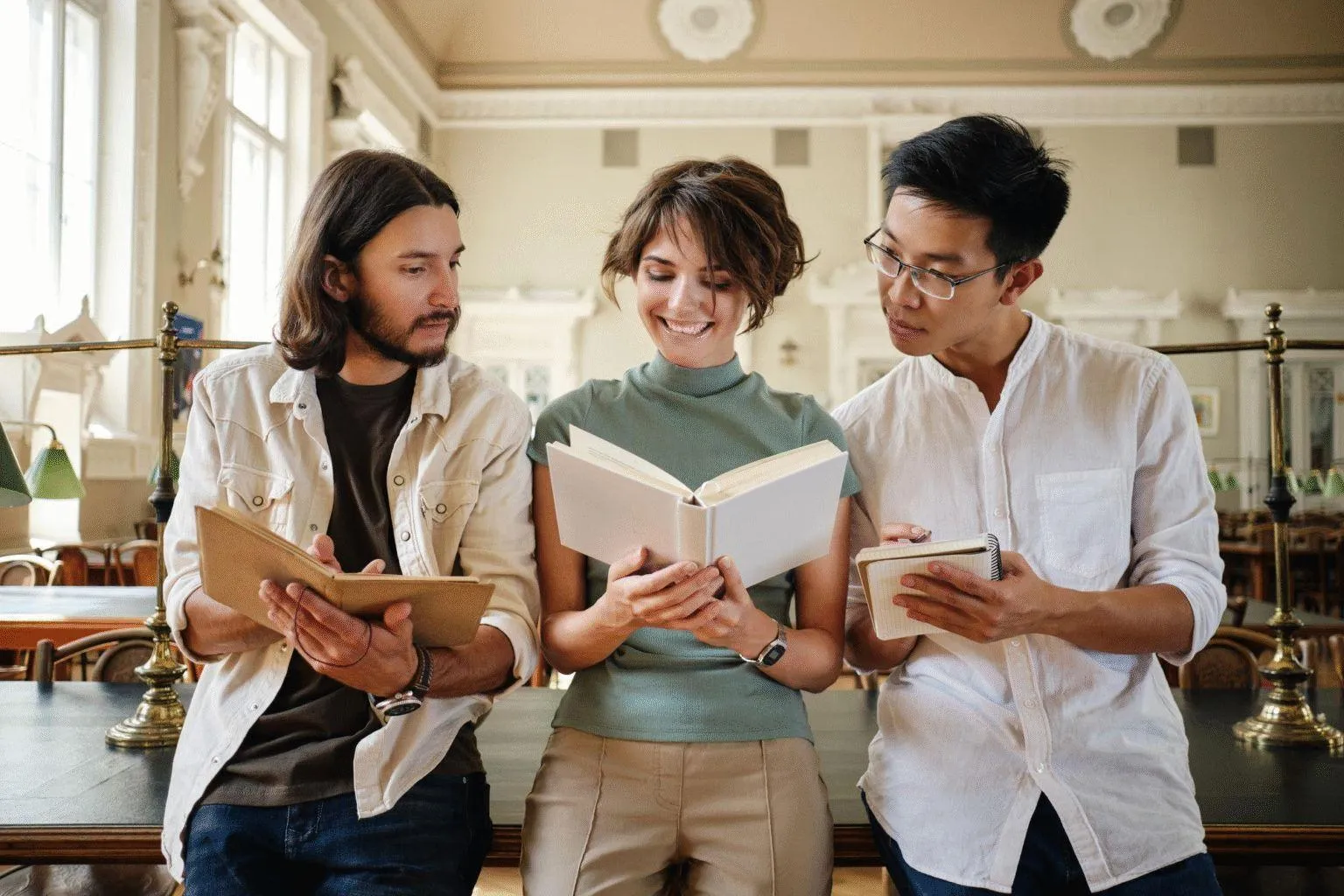 Three young adults reading books together in a bright hall