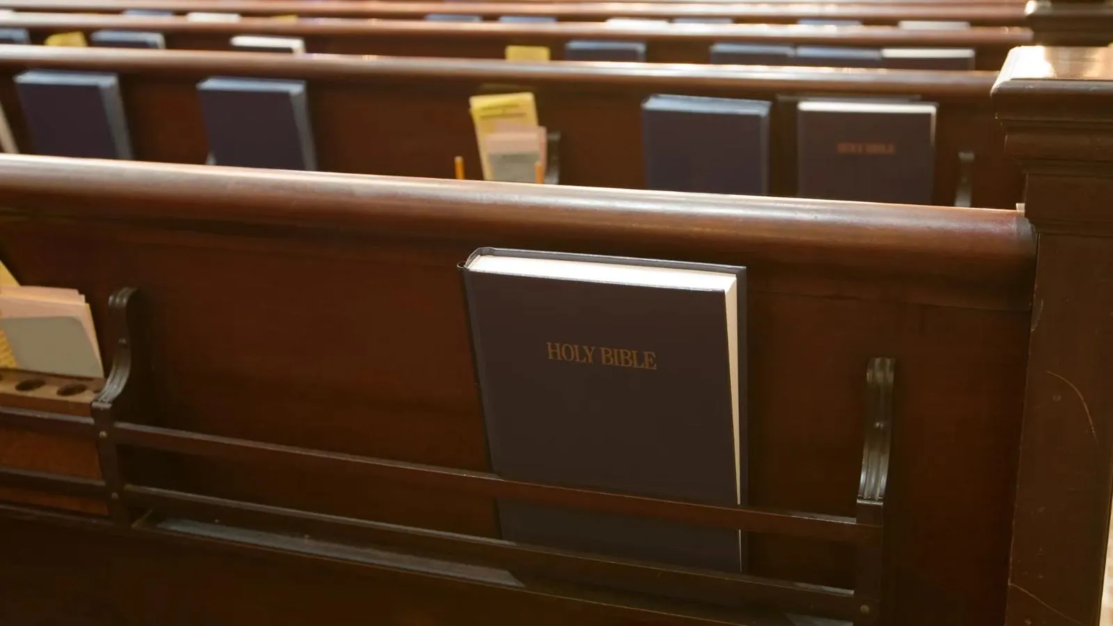 Wooden pews with a Bible in the pew rack